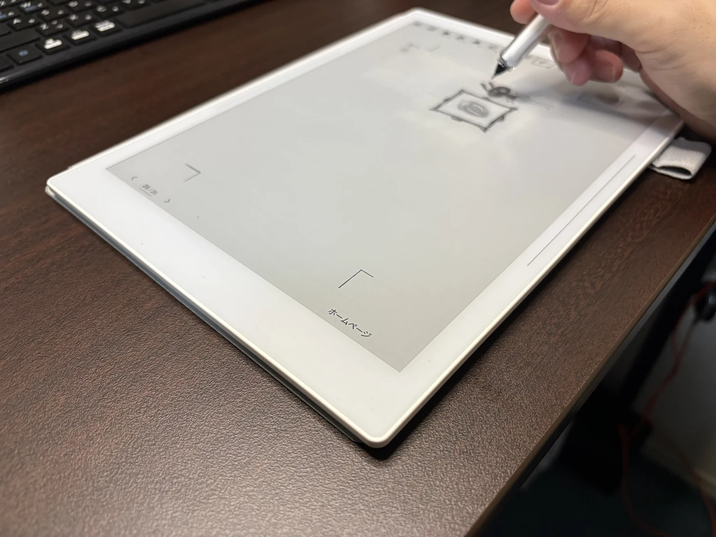 机の上の電子ペーパーにペンで絵を描いている、現在の制作風景